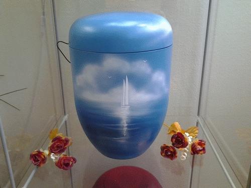 Hellblaue Urne mit weißem Segelschiffmotiv auf offener See.